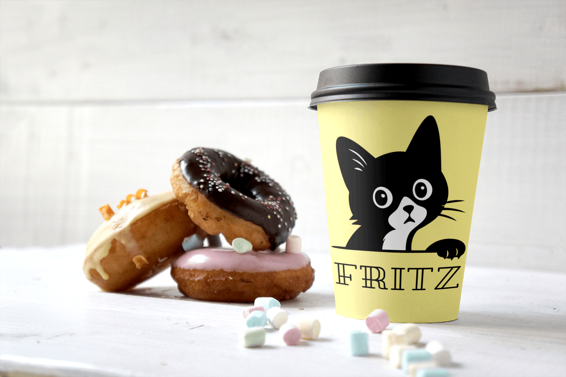 Kaffeebecher mit süßem schwarzen Kater und dem Namen „FRITZ“ – umgeben von Donuts und Marshmallows auf weißem Untergrund. Perfektes Geschenk für Katzenliebhaber,shirt-liebe.de